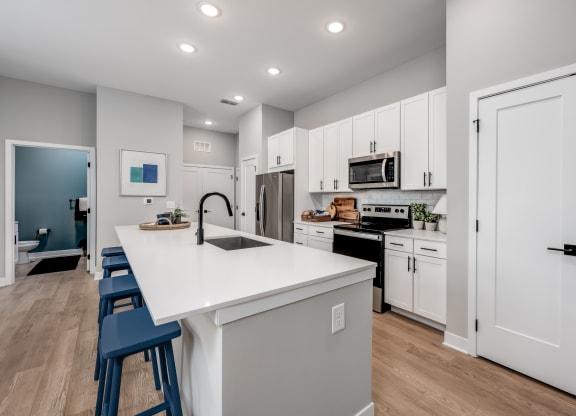 a kitchen with white cabinetry and a large white island with a sink and three stools at Ironwood Flats, Brandon, Florida