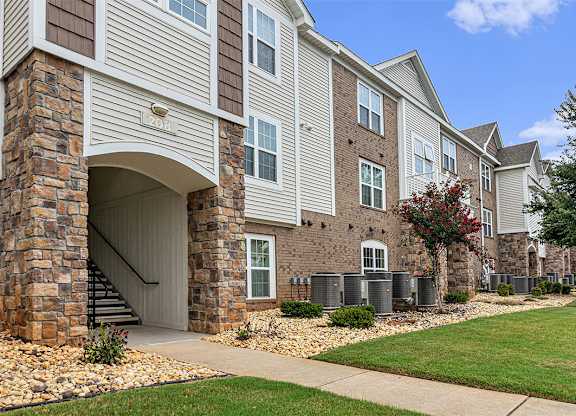 An exterior apartment building with landscaping in front and a clear blue sky above at Limestone Creek Apartment Homes, Madison, AL