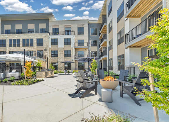 A patio area with chairs and a fire pit in front of apartment buildings at Luxe 360 on Centerpointe Apartments, Virginia, 23114