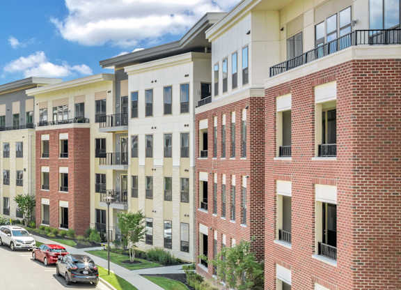 A row of red brick apartment buildings with cars parked in front at Luxe 360 on Centerpointe Apartments, Midlothian, Virginia