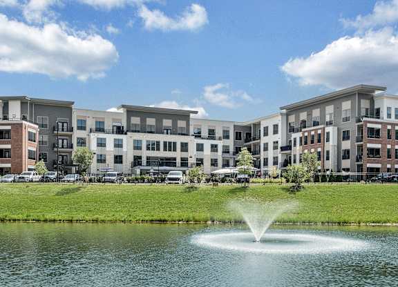 A fountain in the middle of a pond in front of apartment buildings at Luxe 360 Apartment Complex in Midlothian Virginia
