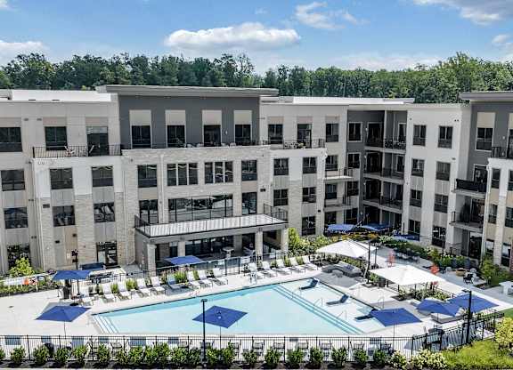 A large swimming pool surrounded by a fence and umbrellas in front of apartment buildings at Luxe 360 Apartment Complex in Midlothian Virginia