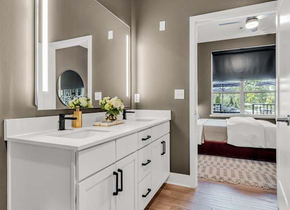 A bathroom with a vanity, mirror, and a bedroom in the background at Luxe 360 on Centerpointe Apartments, Virginia, 23114