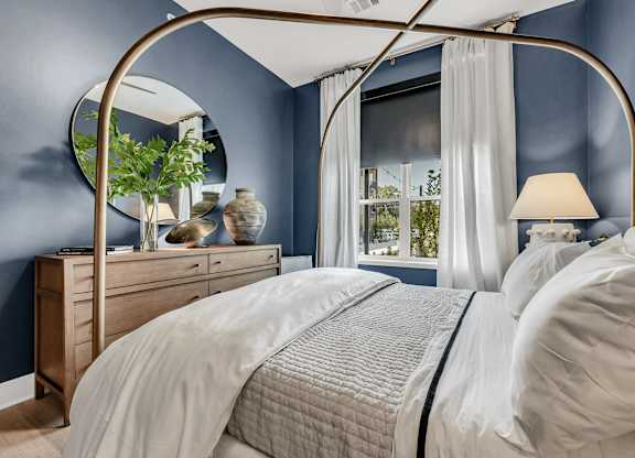 A bed with a canopy and a white bedspread in a room with blue walls at Luxe 360 on Centerpointe Apartments, Virginia