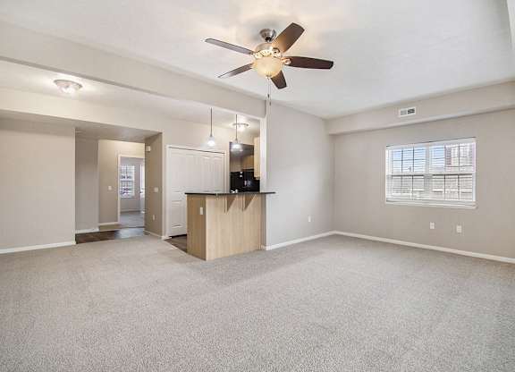 An enlarged living room with a carpeted floor, a ceiling fan, and a window with blinds at Lynbrook Apartments and Townhomes, Elkhorn, NE, 68022