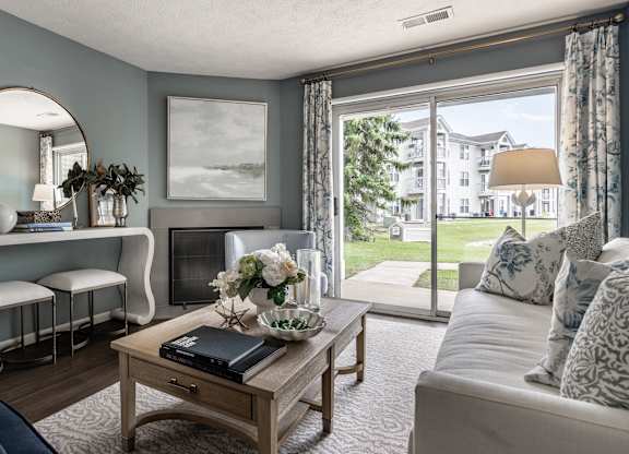 A living room with a sofa, a coffee table, a mirror, and a window with a view of a building at Mallard Bay Apartments, Crown Point, Indiana