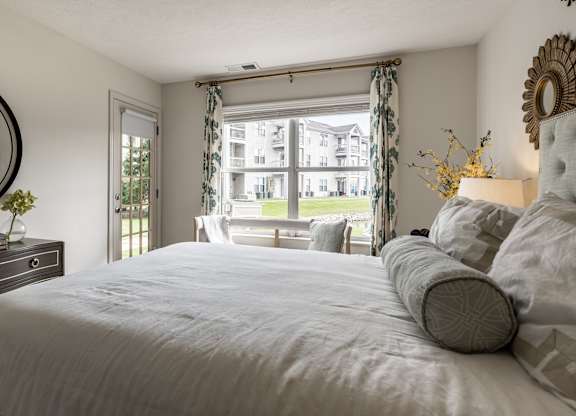 A bedroom with a large bed, a dresser, and a window with curtains at Mallard Bay Apartments, Crown Point, Indiana