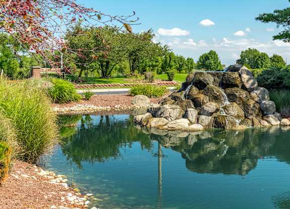 A pond with rocks in the middle  at Mallard Bay Apartments, Crown Point, Indianaand trees in the background