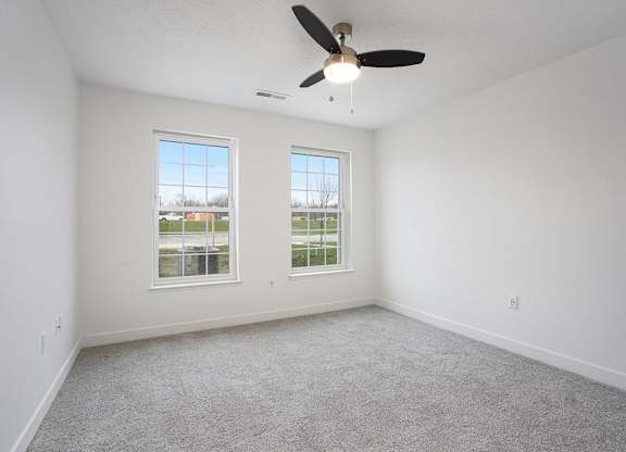 A bedroom with a ceiling fan and two windows at Meadowbrooke Apartment Homes in Kentwood, MI 49512