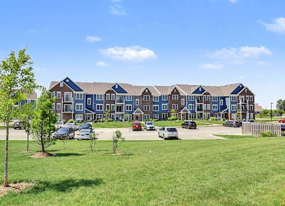 A large apartment building is surrounded by a grassy area and a few trees at Meadowbrooke Apartment Homes in Grand Rapids, MI 49512