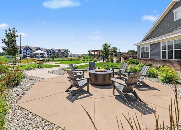 A patio with a fire pit and chairs is surrounded by a grassy lawn at Meadowbrooke Apartment Homes in Grand Rapids, MI 49512