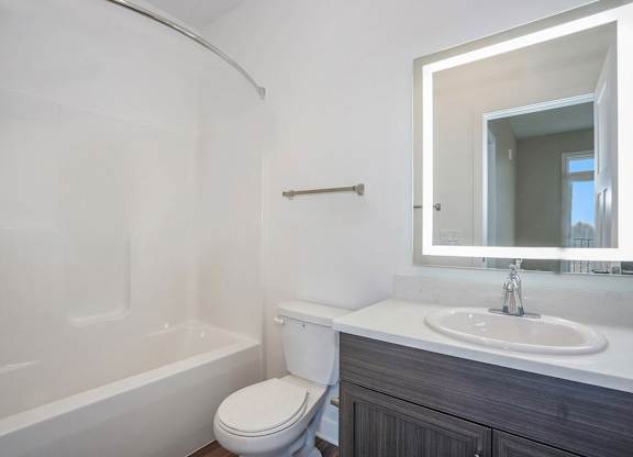 A bathroom with a bathtub, sink, and a lighted mirror at Meadowbrooke Apartment Homes in Kentwood, MI 49512