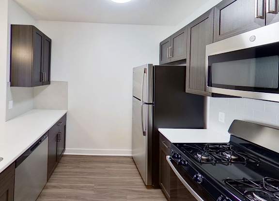 A kitchen with dark brown cabinets and stainless steel appliances at Meadowbrooke Apartment Homes in Kentwood, MI 49512