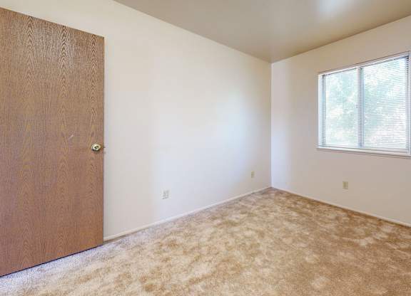 A bright bedroom with a window with blinds at Mount Royal Townhomes, Kalamazoo, MI