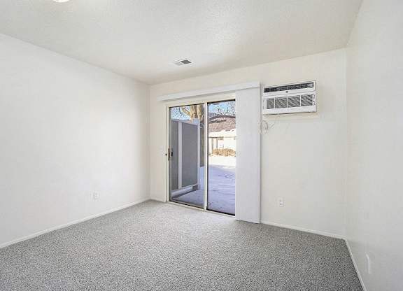 A bedroom with a grey carpet and a slider to a private patio at Newport Village Apartments, Portage, MI