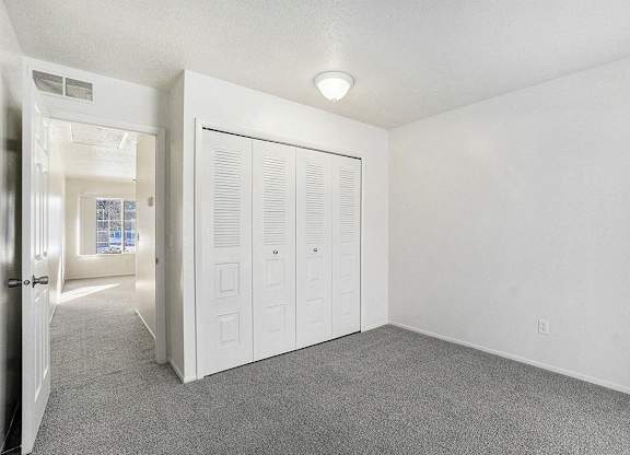 A bedroom with a grey carpet and a closet at Newport Village Apartments, Portage, MI