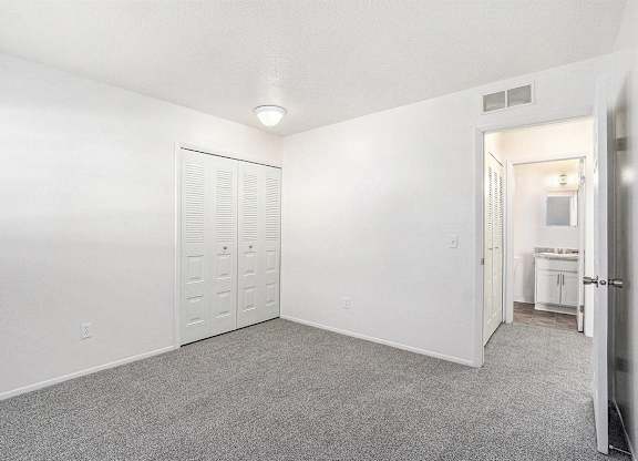 A spacious bedroom with a grey carpet and a closet at Newport Village Apartments, Portage, MI