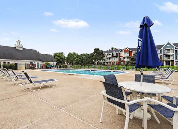 A poolside area with chairs and tables is shown at Newport Village Apartments, Portage, 49002