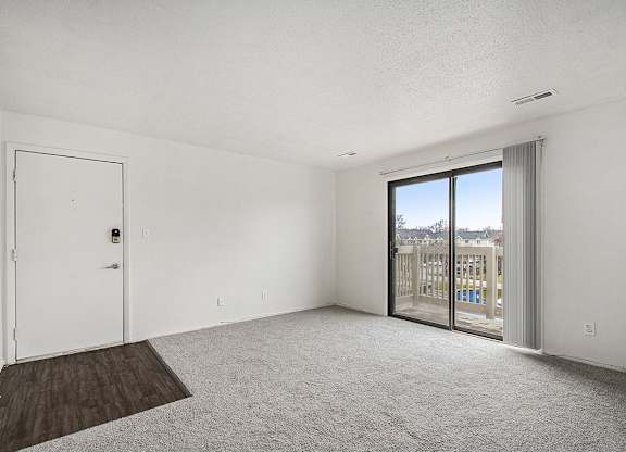 A living room with plush carpet and a slider to a private balcony with a view at Normandy Village Apartments, Michigan City, 46360