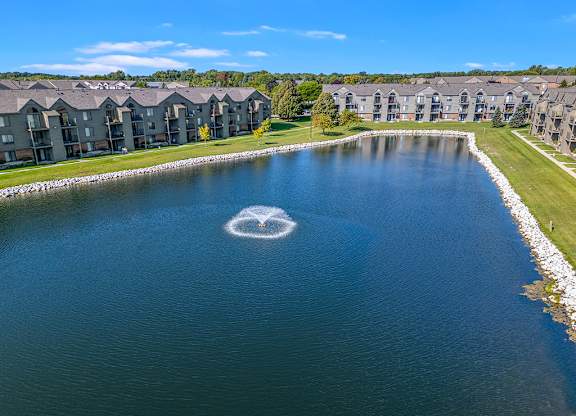 A large pond with a fountain in the middle at Oak Shores Apartments in Oak Creek, WI