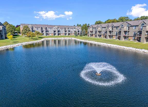 A fountain in the middle of a pond in back of apartment buildings at Oak Shores Apartments in Oak Creek, WI