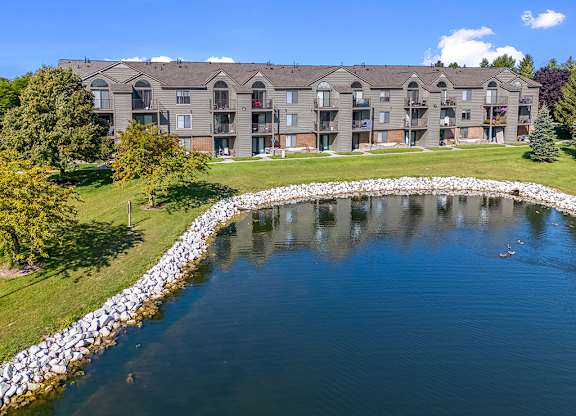 The rear view of a building with a pond in back at Oak Shores Apartments in Oak Creek, WI