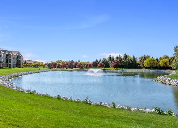 A serene pond surrounded by a well-manicured lawn and a stone wall at Oak Shores Apartments in Oak Creek, WI
