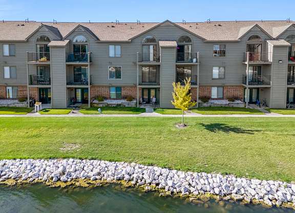 The back of an apartment building with a pond and tree at Oak Shores Apartments in Oak Creek, WI