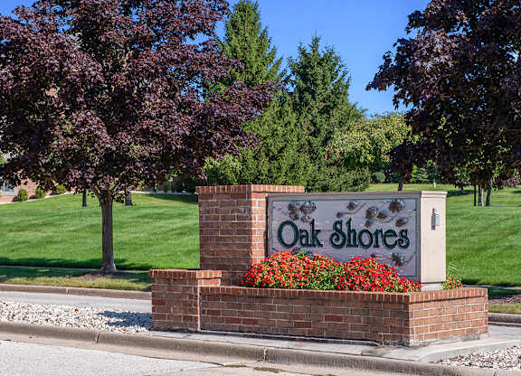 An entrance sign with mature shade trees at Oak Shores Apartments in Oak Creek, WI