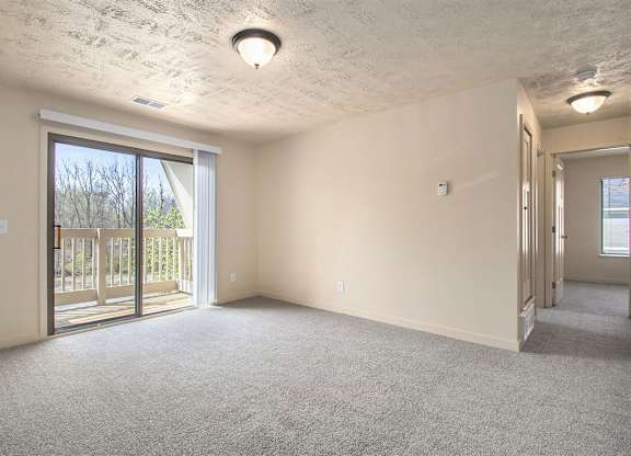 A living room with a carpeted floor and a sliding glass door leading to a balcony at Old Farm Apartments, Elkhart, Indiana