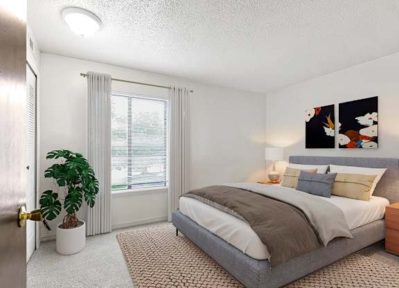A bedroom with a bed, nightstand, window and a plant at Old Monterey Apartments in Springfield, MO