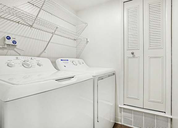 A white dryer and washing machine in a laundry room at Pine Knoll Apartments, Battle Creek