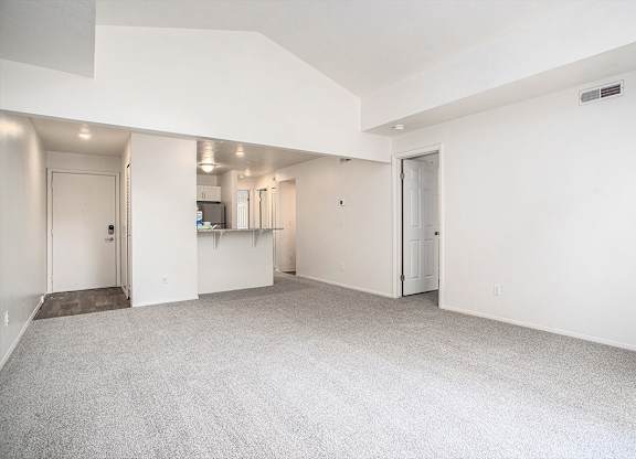 A large, empty living room with a cathedral ceiling and carpeted floor at Pine Knoll Apartments, Battle Creek, 49014