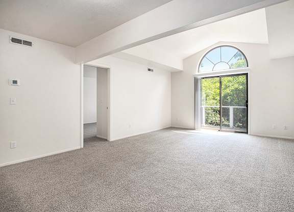 A spacious living room with a large window, cathedral ceiling, and carpeted floor at Pine Knoll Apartments, Battle Creek, 49014