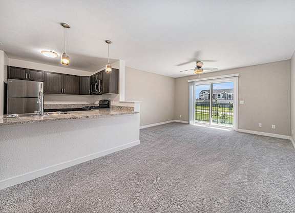 A spacious living room with a kitchen area and sliding glass doors leading to a balcony.