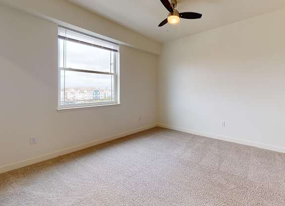 A bedroom with a ceiling fan and a window at The Reserve at Destination Pointe apartments, Grimes, IA