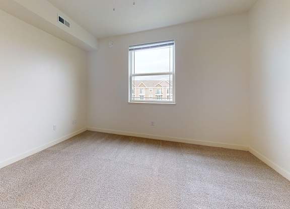 Empty bedroom with carpeted floor and a window at The Reserve at Destination Pointe apartments, Grimes, IA