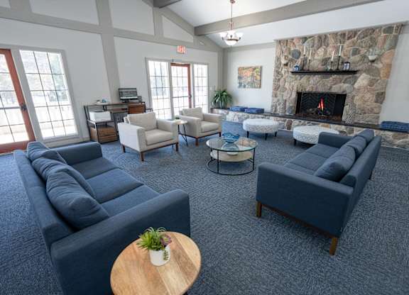 A living room with a stone fireplace and a variety of seating options at Rivers Edge Apartments, Waterford, MI
