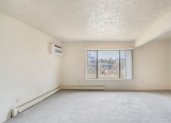 A living room with a large window overlooking a residential area at Seville Apartments, Kalamazoo, MI