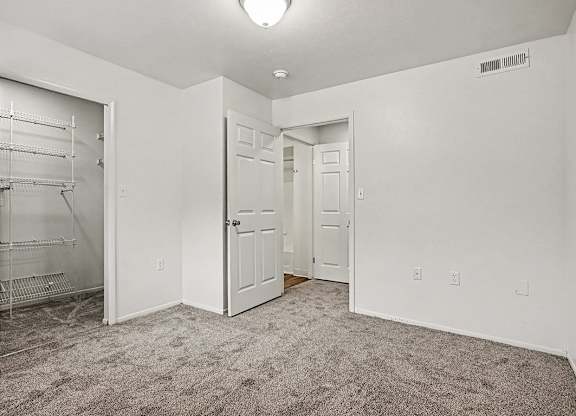 A white room with a carpeted floor and a white closet with shelves.