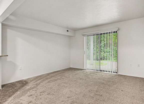 A room with a carpeted floor and a window with blinds.