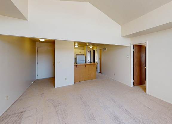 A large empty living room with a high ceiling and a kitchen with a breakfast bar at South Bridge Apartments in Fort Wayne, Indiana