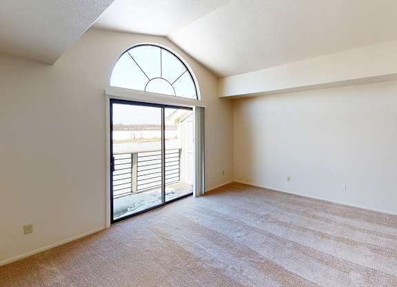 A living room with a cathedral ceiling and large window and sliding glass doors to a balcony at South Bridge Apartments in Fort Wayne, Indiana