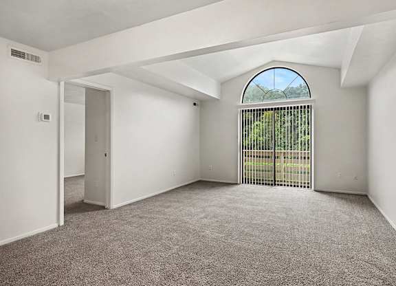 A room with a carpeted floor and a large window with a view of a fence and trees.