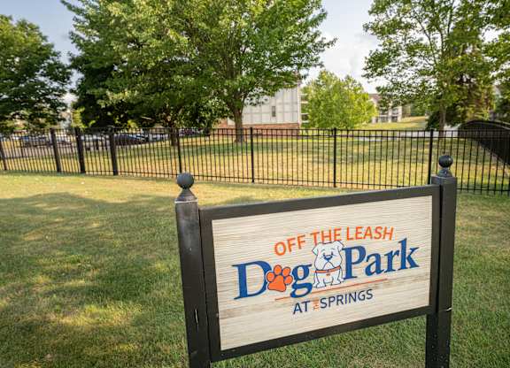 A sign for Dog Park at Springs is displayed in a grassy area.