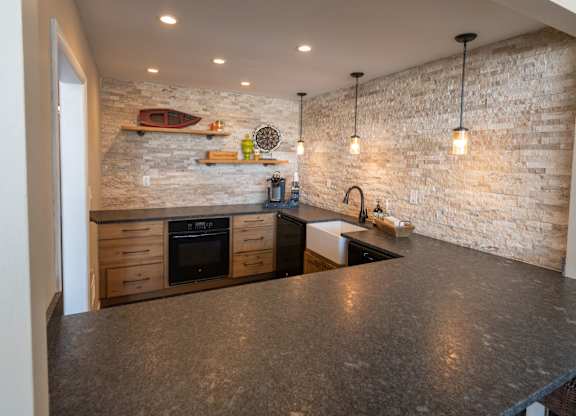 A kitchen with a stone wall and a black counter top.