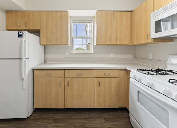 A kitchen with window, wooden cabinets and white appliances at Stoney Pointe Apartment Homes, Kansas