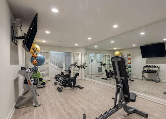 A well-equipped home gym with various exercise machines and a flat-screen TV mounted on the wall. at Sundance Apartments, Indiana