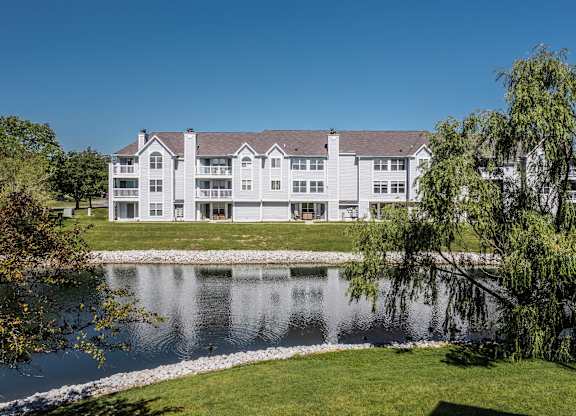 A large white building with a grey roof is situated next to a body of water. at Sundance Apartments, Indiana, 46237