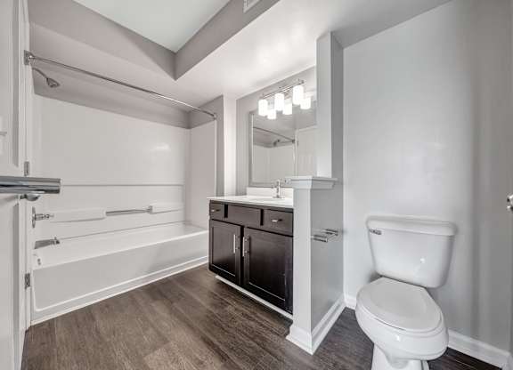 A white toilet sits in a bathroom with a wooden floor and white walls. at Sunscape Apartments, Roanoke, 24018